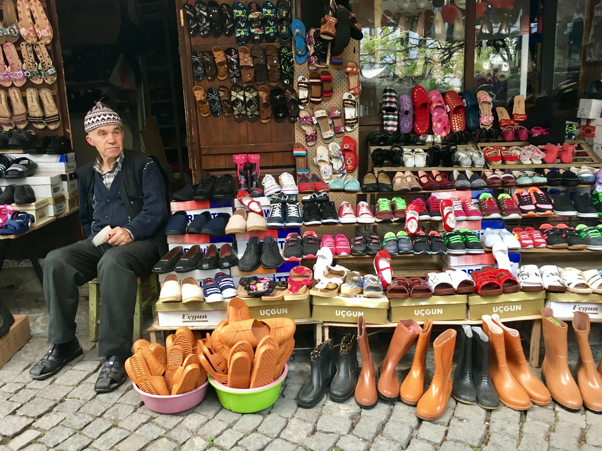 A vibrant display of various shoes at an outdoor market in Turkey with a vendor sitting beside.